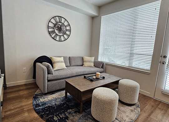 A living room with a grey couch, a coffee table, and a clock on the wall.