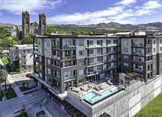 A large apartment complex with a pool and a view of a church and mountains in the background.