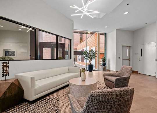 A modern living room with a white sofa, brown wicker chairs, and a large window.