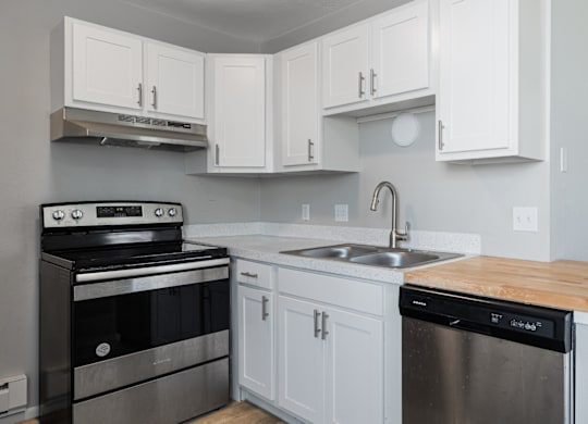 A kitchen with a stove, sink, and cabinets.