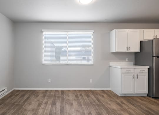 A kitchen area with a refrigerator, cabinets, and a window with blinds.