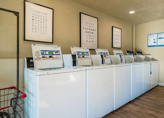 A laundry room with a row of washing machines and a shopping cart.