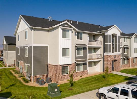A white car is parked in front of a two-story apartment building.