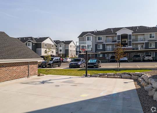 A parking lot in front of apartment buildings with cars parked.