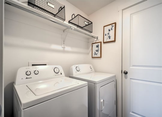 a white laundry room with two washes and a dryer at Aderra apartment complex in Roy, Utah