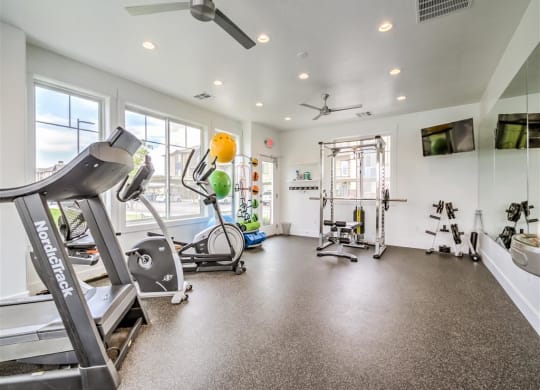 a gym with various exercise equipment and windows at Aderra apartment complex in Roy, Utah