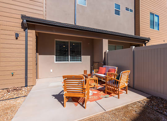 A patio with a table and chairs is in front of a tan building.