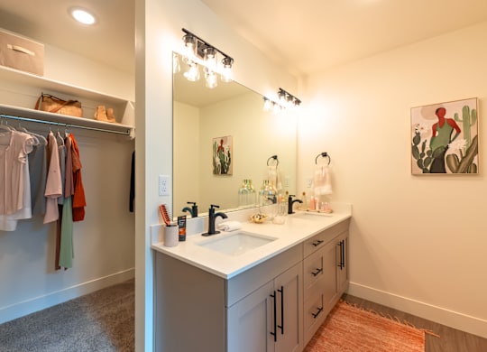 A bathroom with a sink, mirror, and clothes hanging up.