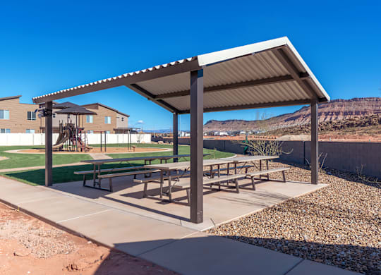 A covered picnic area with tables and benches is situated in a sunny outdoor setting.