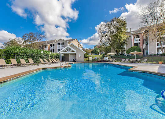 a swimming pool with chairs and umbrellas in front of a house at Arbors at Windsor Lake, Columbia, SC  