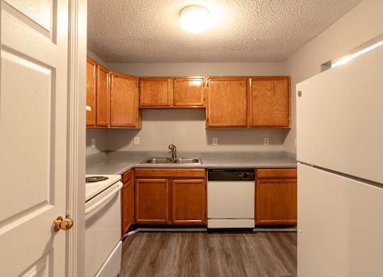 an empty kitchen with white appliances and wooden cabinets at Avon Crossings, Durham, NC 27713