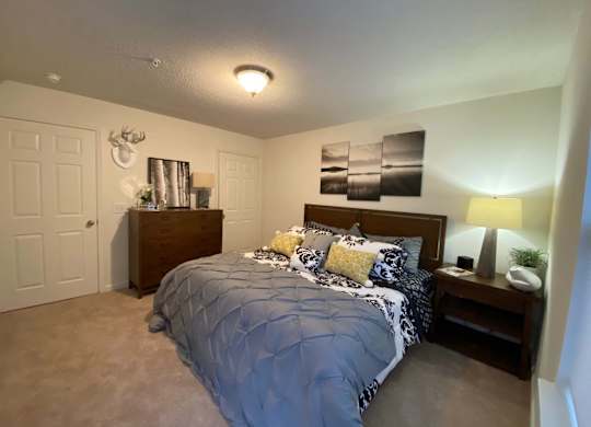 A bedroom with a bed, nightstand, and a deer head on the wall.