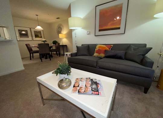 A living room with a grey couch, a white coffee table, and a painting on the wall.