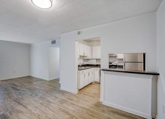 an empty living room with a kitchen in the background
