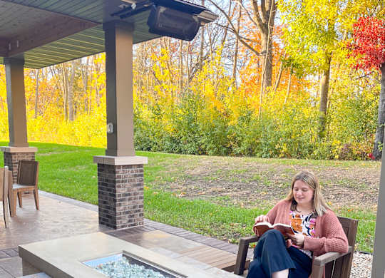 A woman is sitting on a chair on a patio with a fire pit in front of her.