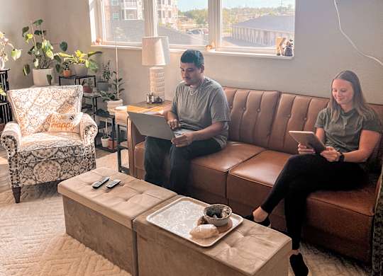 Two people sitting on a couch in a living room with a coffee table in front of them.