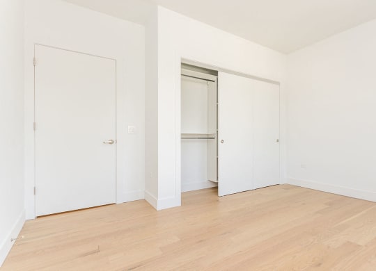 a bedroom with white walls and wood floors and a closet