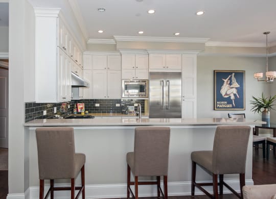 a kitchen with white cabinets and a bar with chairs