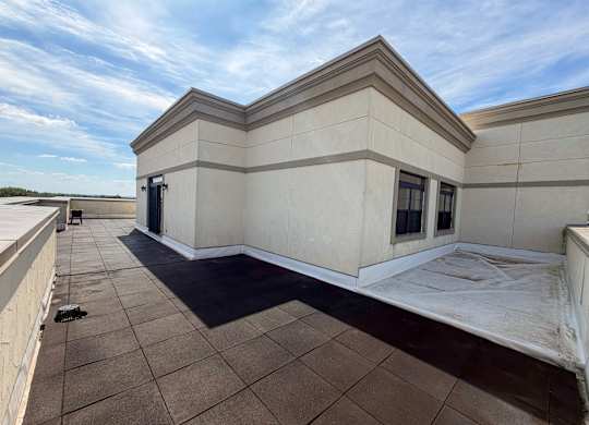 A large, empty patio area with a tiled floor and a building with a flat roof in the background.