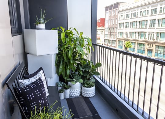 a small balcony with plants and a black and white pillow