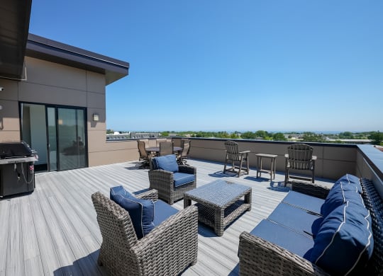 a rooftop deck with wicker furniture and a grill