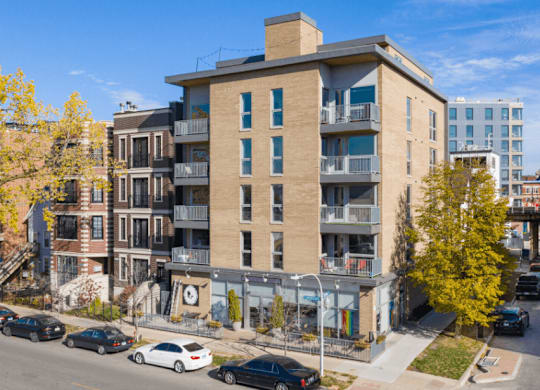 A street view of a residential area with cars parked on the side of the road and apartment buildings in the background.