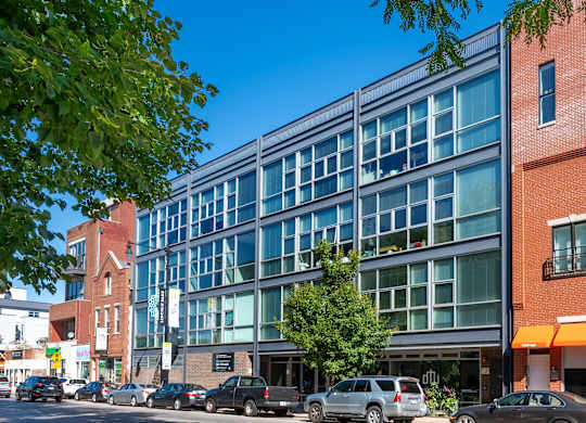 A modern glass building is situated on a street corner with cars parked in front.