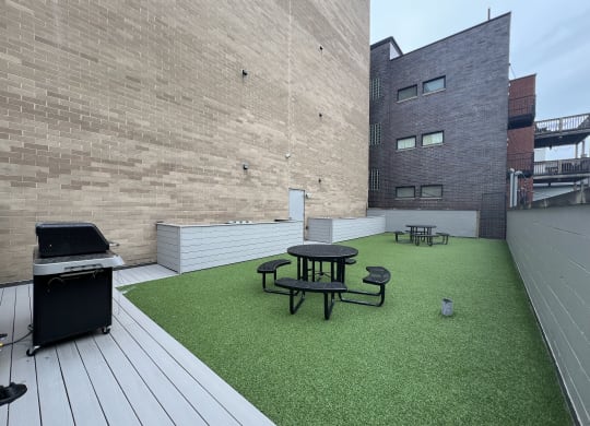 a roof deck with a grill and a table and chairs on a green turf