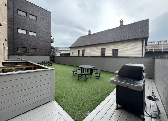 a roof deck with a grill and a picnic table on a green turf