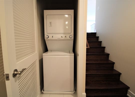 a small washing machine and dryer are tucked under the stairs in a laundry room