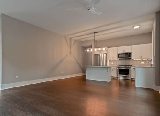 an empty living room with a kitchen in the background
