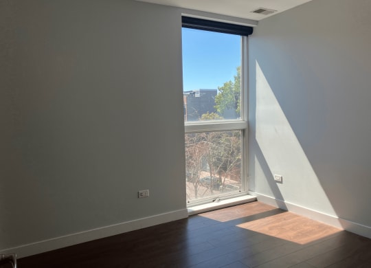 an empty living room with a large window and wooden floors