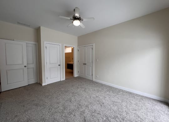 an empty living room with white doors and a ceiling fan