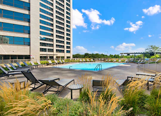 A pool surrounded by chairs and tall grass.