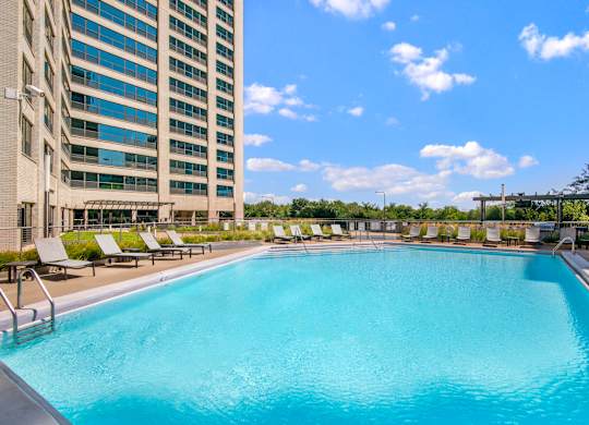 A large swimming pool with sun loungers and a tall building in the background.