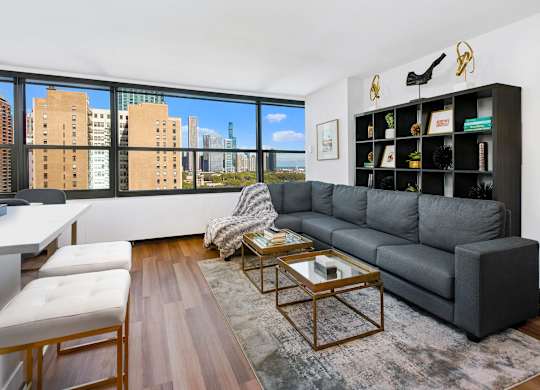 A living room with a grey couch, a coffee table, and a large window with a view of the city.