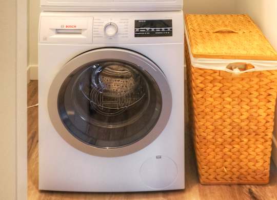 A white washing machine and dryer stacked on top of each other with a yellow laundry basket to the side.