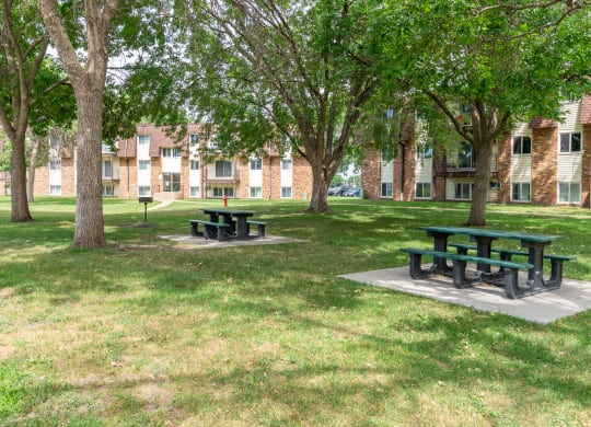 two picnic tables in a grassy area in front of a brick building