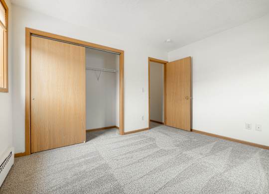 a bedroom with a carpeted floor and two closet doors at Ames Lake Neighborhood Apartments, St. Paul, MN, 55106