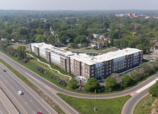 A large building with a white roof is surrounded by trees and a highway.