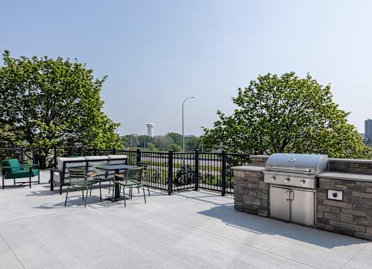 A BBQ grill is on a patio with a table and chairs.