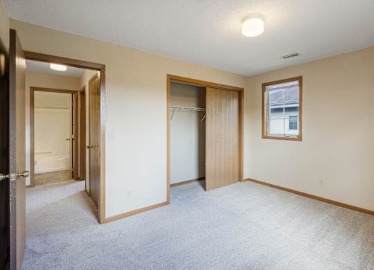 A room with a carpeted floor and a window with a picture frame hanging on the wall.