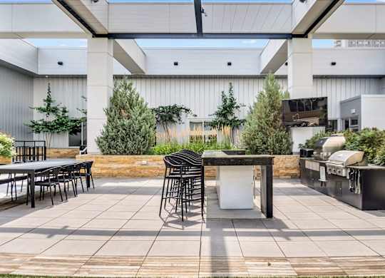 A patio with a table and chairs is surrounded by green plants.
