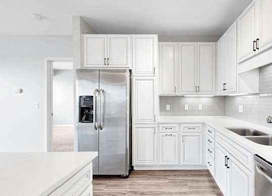 A white kitchen with a refrigerator, cabinets, and a sink.