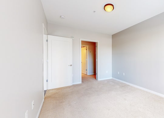 a bedroom with white walls and carpet and a door to a closet
