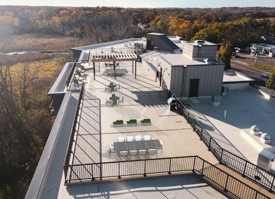 A rooftop patio with a black railing and a few chairs and tables.