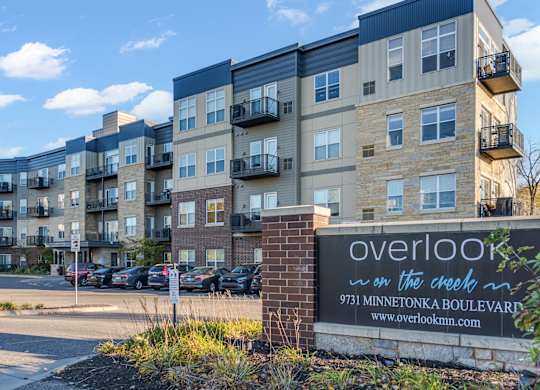 The image shows a multi-story residential building with a sign in front that reads