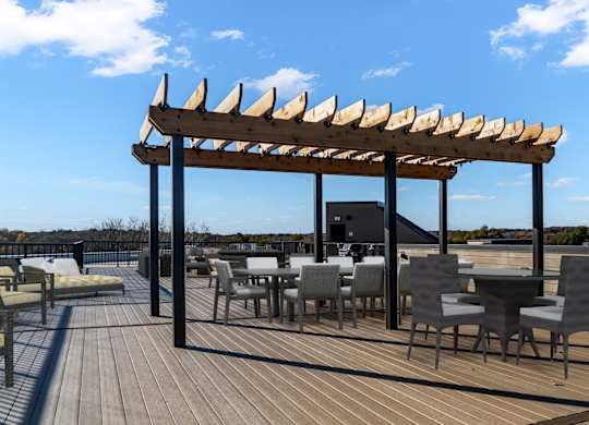 A wooden deck with tables and chairs under a pergola.