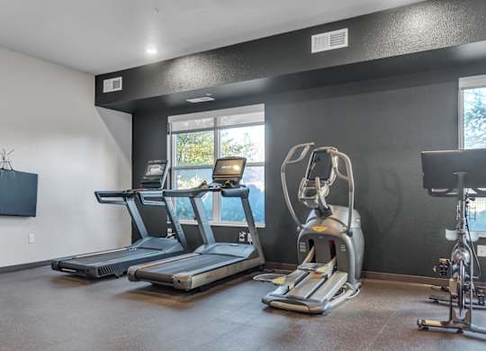 A gym room with treadmills, exercise bikes, and a television.
