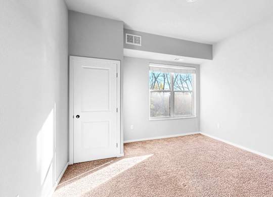 A room with a white door and a window with a view of trees.
